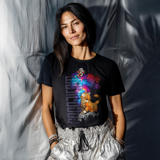 Schwarzes T-Shirt von GOGOJIFAM mit dem Motiv COSMO CAT: Eine langhaarige Ginger-Katze thront auf einem Meteoriten und spielt mit einem Schnürchen. Am anderen Ende schwebt ein hilfloser Astronaut. Das Design im realistischen Comic-Stil verbindet niedliche Anarchie mit kosmischer Überlegenheit und setzt ein augenzwinkerndes Zeichen für Umwelt- und Tierschutz. Denn selbst im All gilt: Natur lässt sich nicht zähmen.